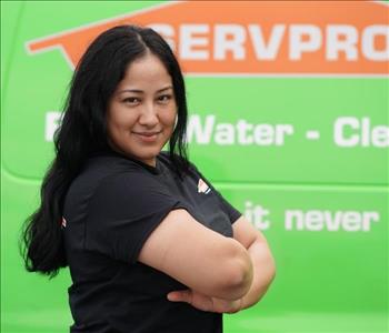 female employee with long black hair wearing a black shirt standing next to a SERVPRO truck
