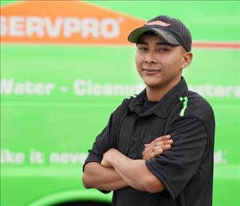Young, clean-shaven man wearing a black hat and SERVPRO hoodie, standing next to a SERVPRO truck