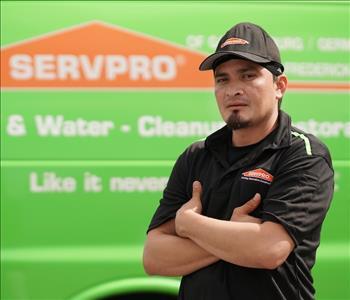 Younger man with a slight beard wearing a black hat and SERVPRO shirt, by a SERVPRO truck