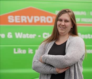 female employee with long hair wearing a grey sweater standing next to a SERVPRO truck