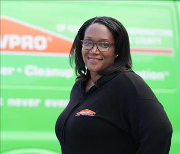 female employee with black hair and glasses standing next to a SERVPRO truck