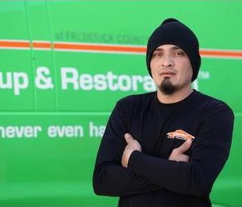 Younger man with a slight beard wearing a black watch cap and long-sleeved SERVPRO shirt, by a SERVPRO truck