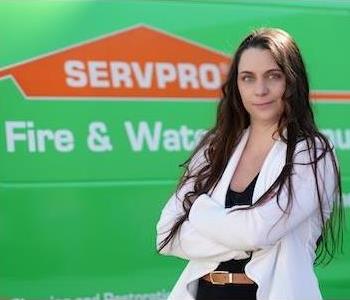 Tall, slender woman with long dark hair and green eyes wearing a white sweater and a slight smile by a SERPRO truck