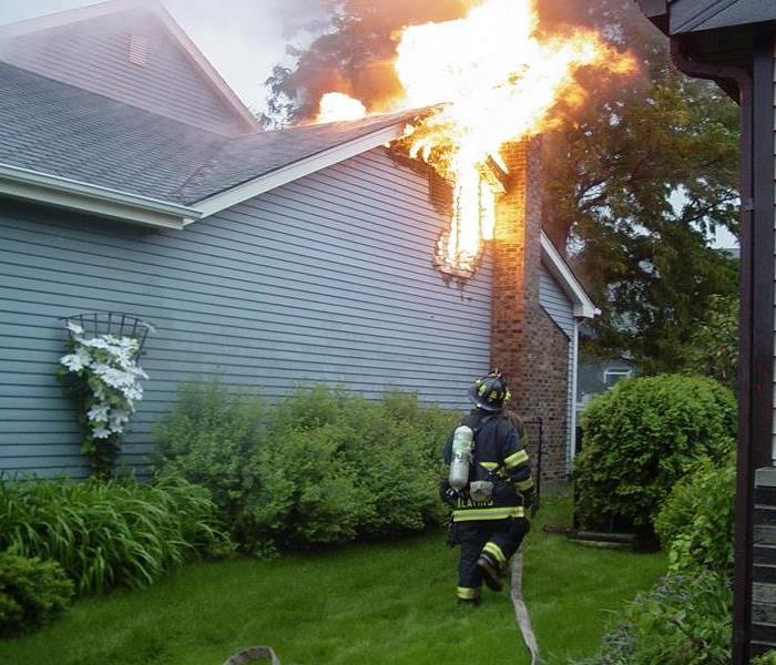 A fireman spraying water on a blue home that is on fire