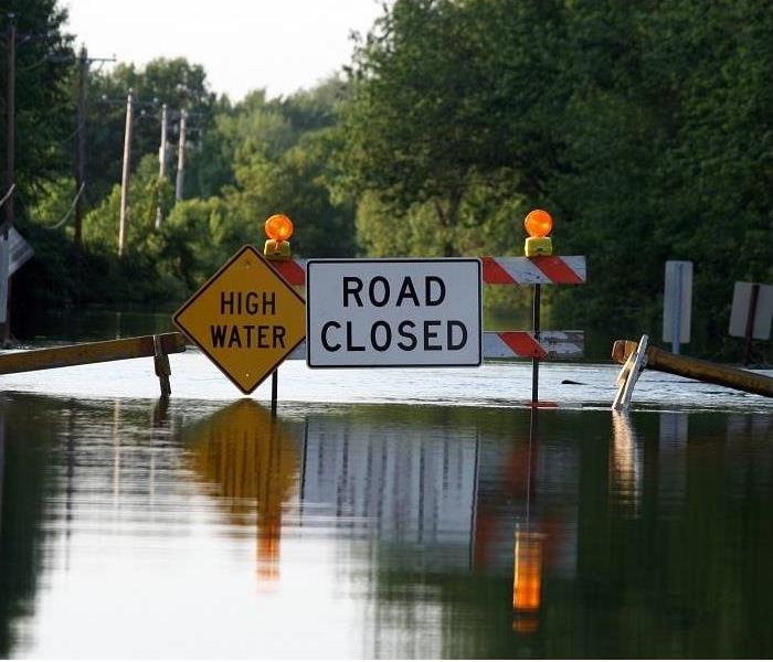 flooded street with 'high water' and 'road closed' signs
