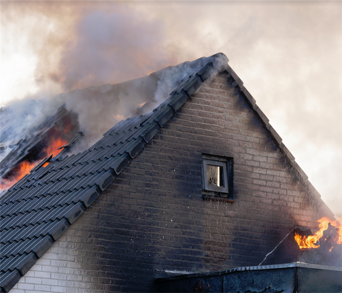 a fire damaged house with smoke and fire billowing from the roof