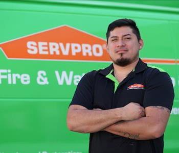 Stout young man with dark hair and chin beard wearing a logo golf shirt, standing with arms folded next to a SERVPRO truck